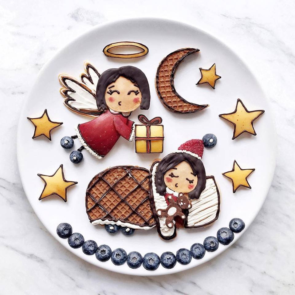 Scena natalizia su piatto, con angelo, luna, stelle e bimba addormentata realizzati con biscotti, cioccolato e frutta
