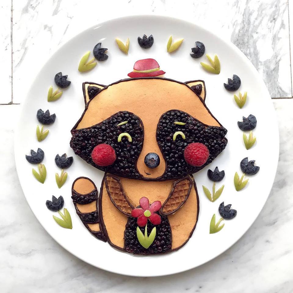 Illustrazione di un orsetto lavatore realizzato con pancake, more, lamponi e decorazioni di frutta