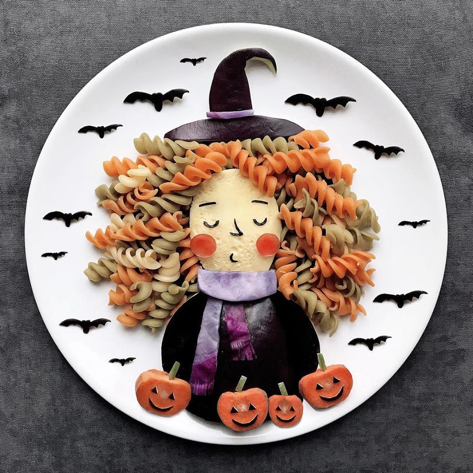 Streghetta di Halloween realizzata con pasta colorata, melanzana e verdure, con zucche e pipistrelli come decorazioni